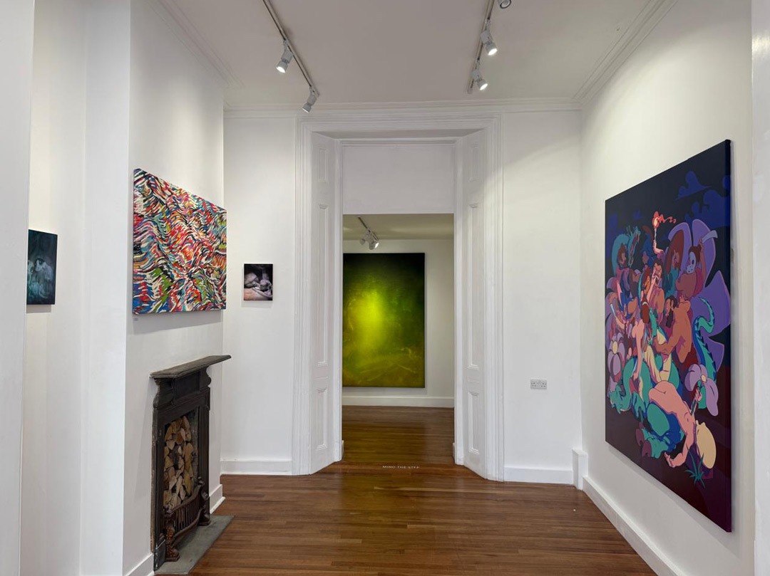 Installation view of Terraforming at Museum Street, Bloomsbury, 2025. Gallery corridor with Victorian fireplace; a large luminous yellow-green painting visible in the back room. Right wall: Nelson Hernández's large figurative painting on dark ground. Multicolour abstract work on the left wall.