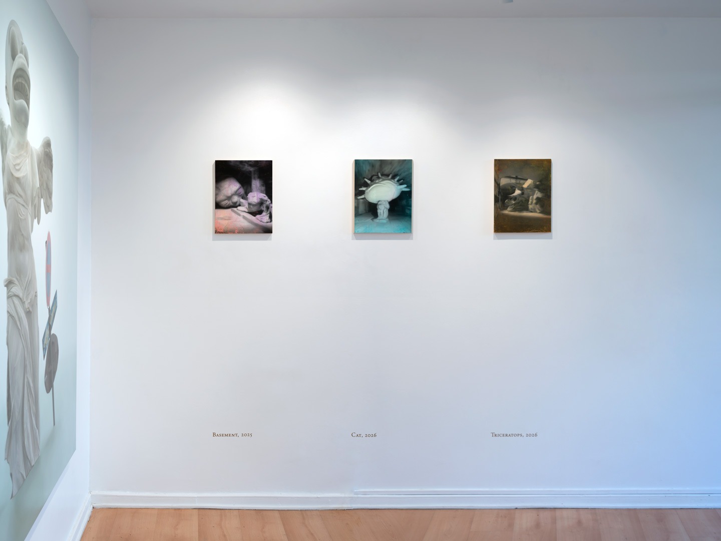 Close-up of three paintings in the main room — Basement, Cat, and Triceratops — with the edge of Victoria visible on the left