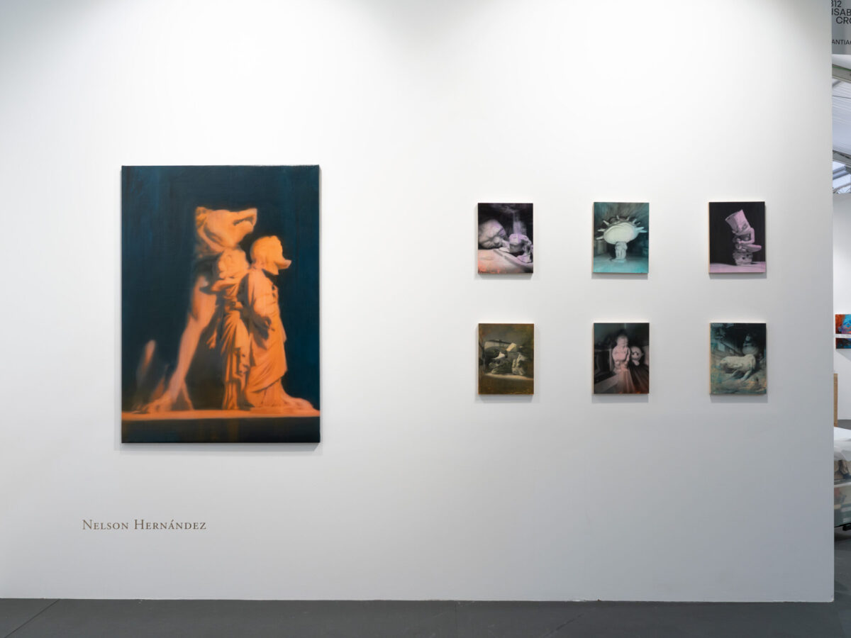 Vista frontal del muro de Nelson Hernández en el stand B-12, Isabel Croxatto Galería, CAN Art Fair Madrid 2026, con una pintura grande de figuras clásicas en tonos ámbar y seis pinturas pequeñas de la serie Fever Dreams dispuestas en grilla