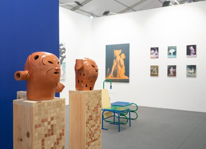 Two large terracotta ceramic head sculptures on tiled wooden plinths in the foreground, with Nelson Hernández's paintings visible in the background at Isabel Croxatto Galería stand, CAN Art Fair Madrid 2026