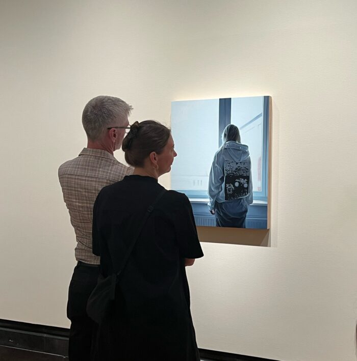 Dos visitantes frente a la pintura Ukranian girl en la galería, observando la composición de la joven de espaldas junto a la ventana con marco institucional visible